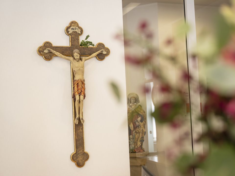 Ein Kruzifix an der Wand, mit großem Blumenstrauß