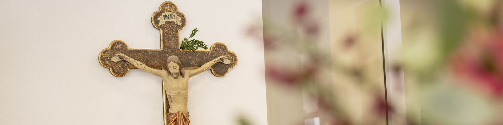 Ein Kruzifix an der Wand, mit großem Blumenstrauß