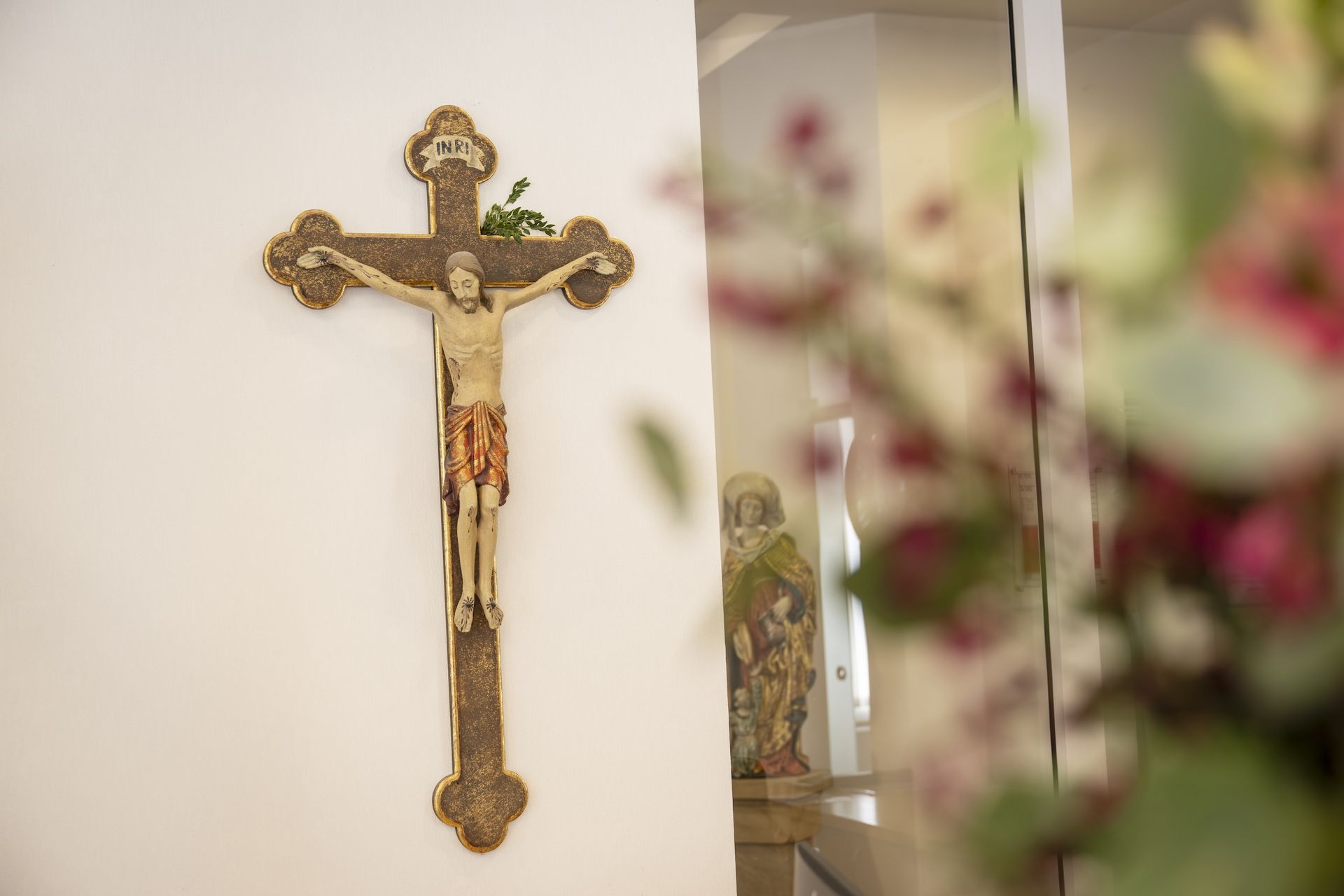 Ein Kruzifix an der Wand, mit großem Blumenstrauß